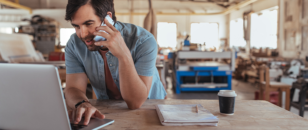 Man talking on the phone while also looking at a laptop.