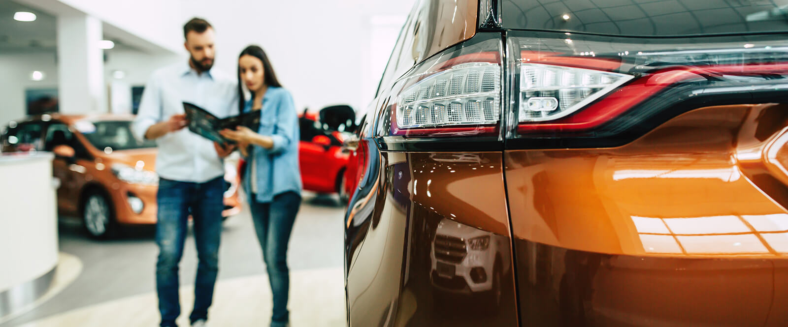 A couple looking at a folder in a car dealership showroom.